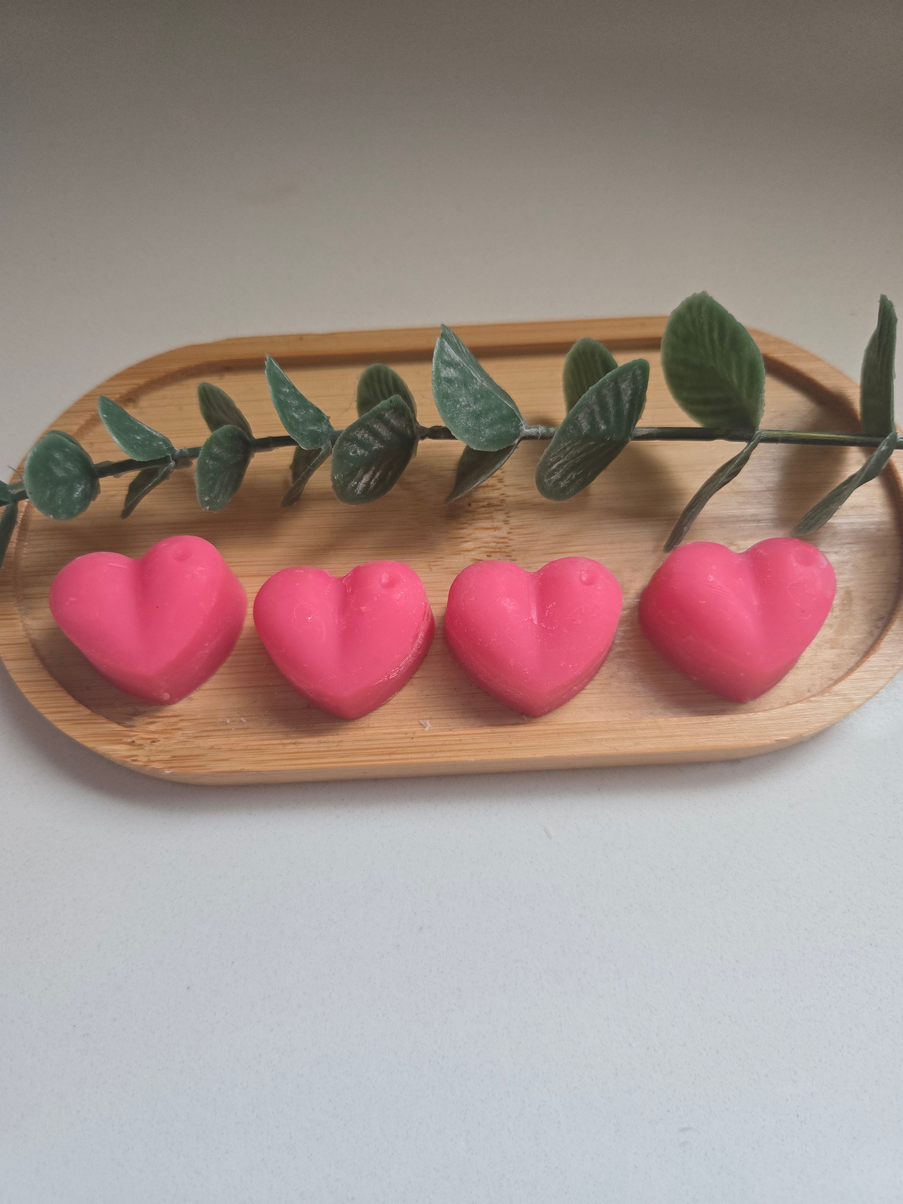 Four pink heart-shaped wax melts on a wooden tray - colours may vary