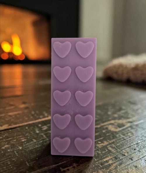 Purple heart wax melt snap bar standing upright in front of a warm fireplace - colours may vary